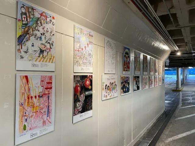 A row of children's drawings of Chinatown scenes mounted on a white wall along a garage driveway
