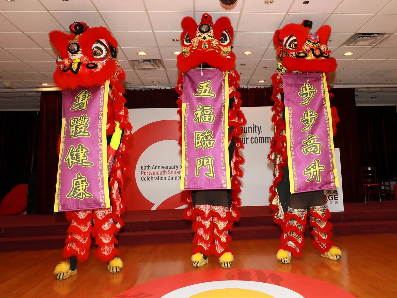 Three lion dancers holding banners of good wishes on stage at the 60th Anniversary Gala