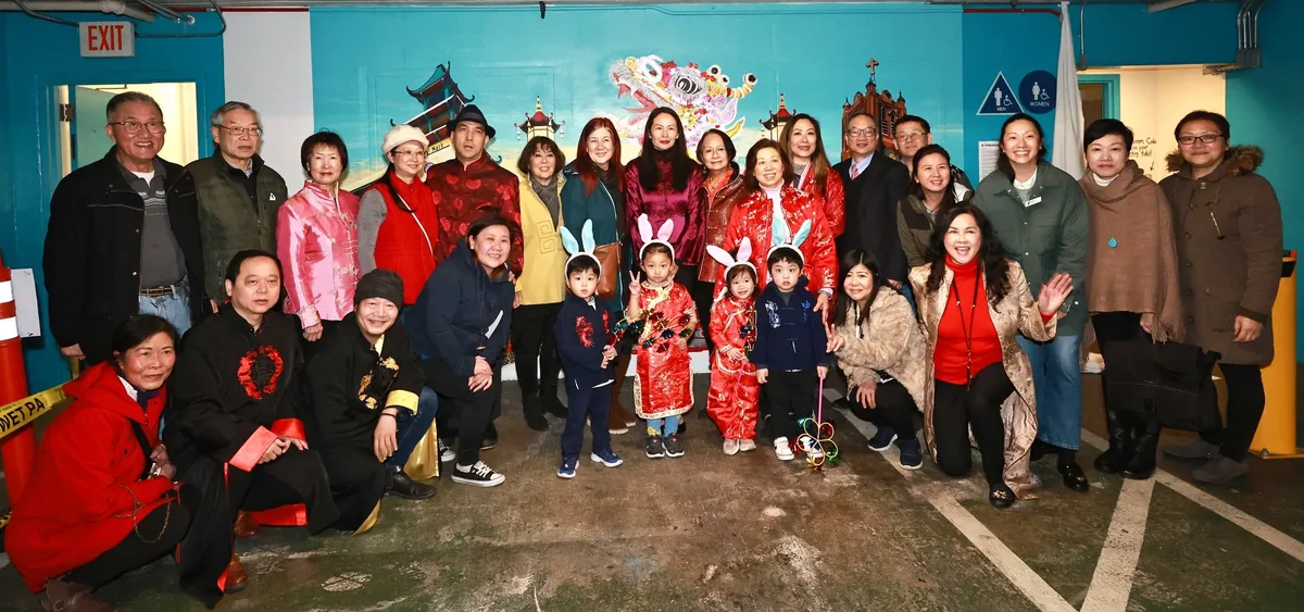 A large group of adults and children in festive clothing, some wearing rabbit ears, in front of the unveiled mural