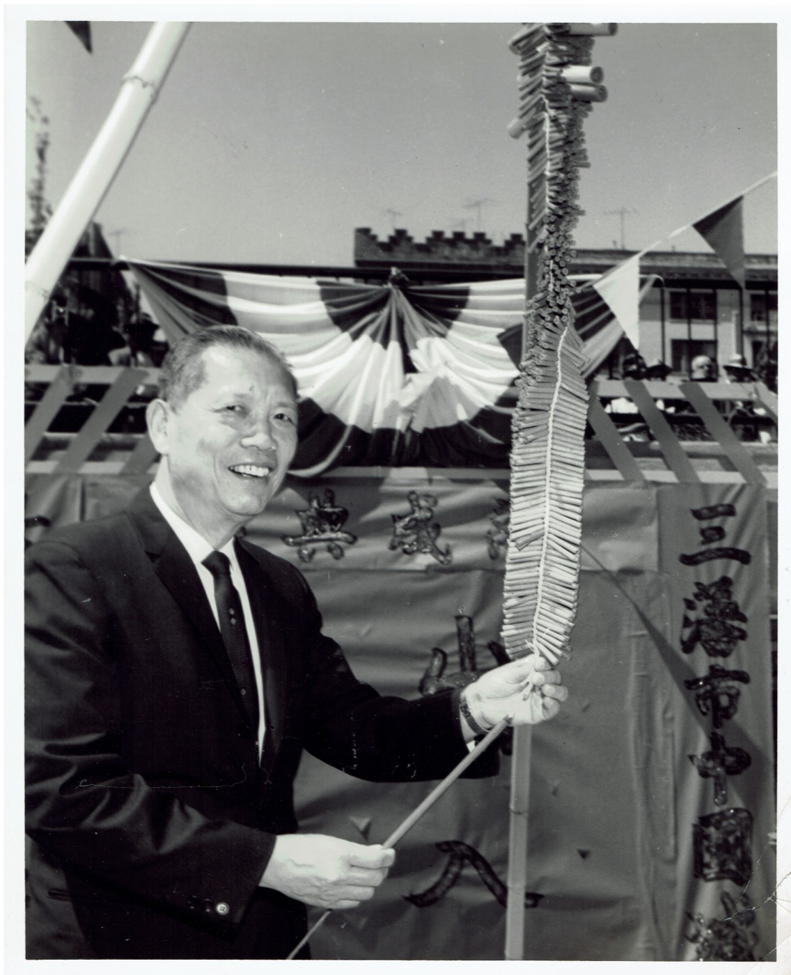 Historic Chinatown photograph by Chin Mon Wah: a man lighting a long string of firecrackers at a celebration