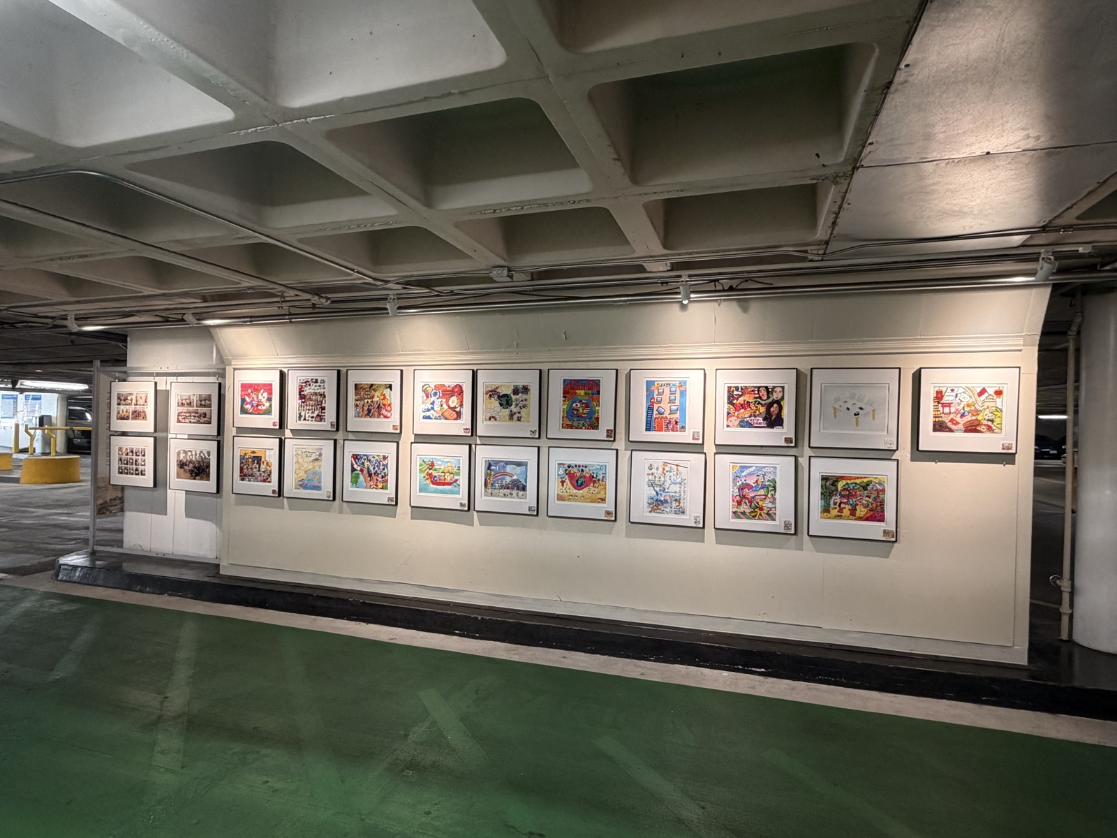 Two rows of framed, brightly coloured children's artworks on a lit white wall inside the garage